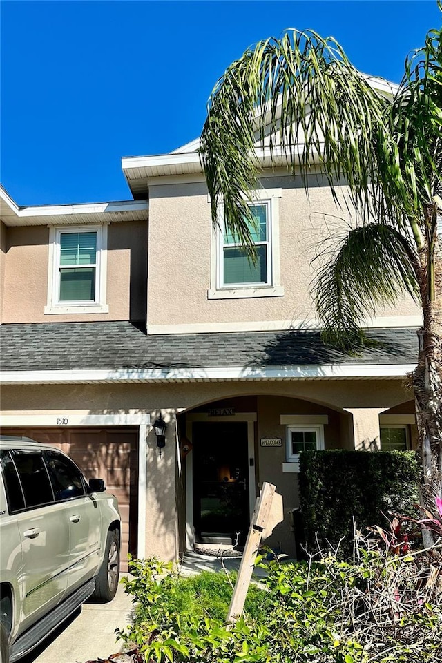 townhome / multi-family property with a garage, roof with shingles, and stucco siding