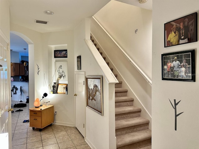 stairway with arched walkways, tile patterned flooring, baseboards, and visible vents