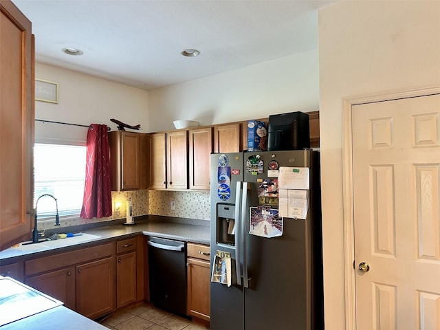 kitchen with light tile patterned floors, a sink, stainless steel refrigerator with ice dispenser, dishwasher, and dark countertops