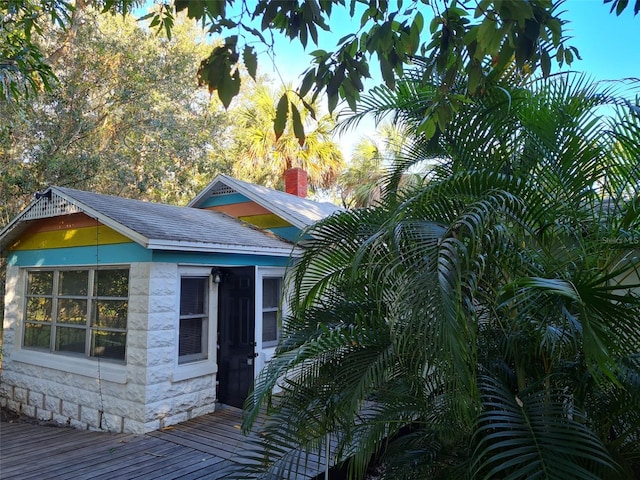 view of property exterior with stone siding, a chimney, a deck, and roof with shingles