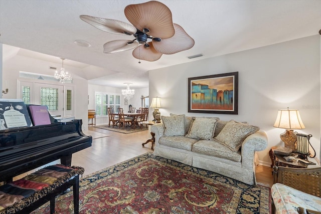 living area with visible vents, wood finished floors, and ceiling fan with notable chandelier