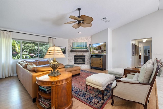 living room featuring a fireplace, light wood finished floors, lofted ceiling, visible vents, and ceiling fan