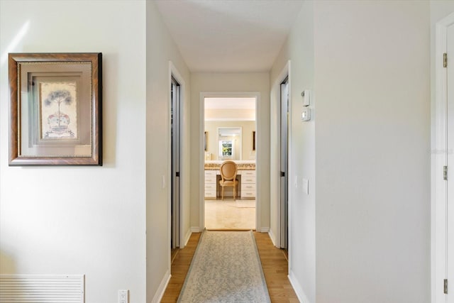 hall featuring light wood-style floors, visible vents, and baseboards