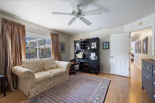 living area with a textured ceiling, ceiling fan, light wood-style flooring, and baseboards