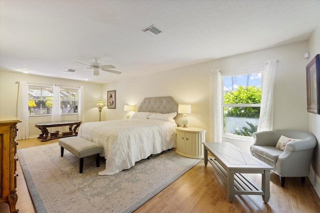 bedroom with light wood finished floors, multiple windows, visible vents, and a ceiling fan