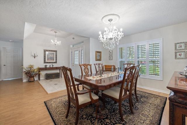 dining area featuring a textured ceiling, light wood-style floors, baseboards, and a notable chandelier