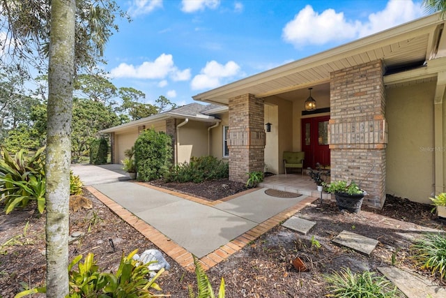 view of exterior entry featuring a garage, brick siding, and stucco siding