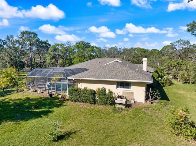 back of house featuring a yard, a chimney, stucco siding, a shingled roof, and a lanai