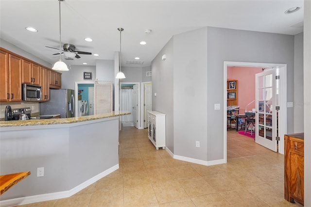 kitchen featuring light stone counters, brown cabinets, stainless steel appliances, ceiling fan, and washer / dryer