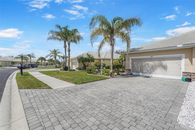 ranch-style home featuring decorative driveway, stucco siding, a garage, a tiled roof, and a front lawn