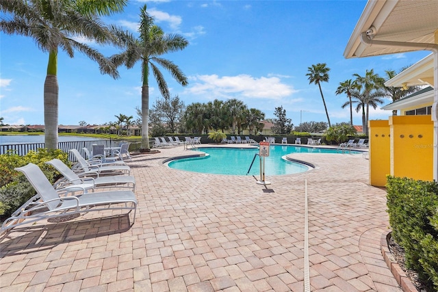 community pool with a patio area, fence, and a water view