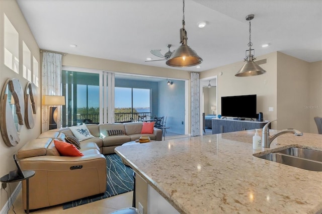 kitchen featuring light stone counters, decorative light fixtures, recessed lighting, open floor plan, and a sink