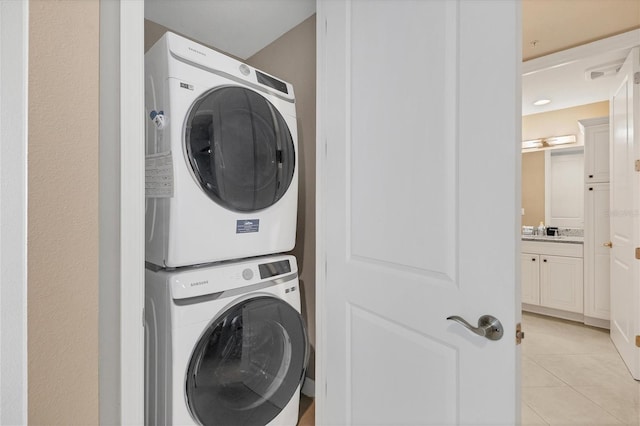 laundry area with stacked washer and dryer, laundry area, a sink, and light tile patterned flooring