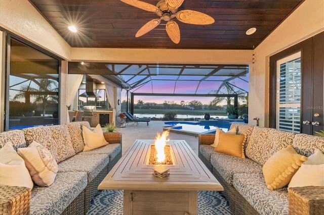 patio terrace at dusk featuring an outdoor pool, glass enclosure, an outdoor living space with a fire pit, and a ceiling fan