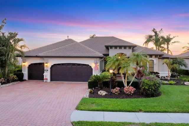 view of front facade with stucco siding, a lawn, a tile roof, decorative driveway, and an attached garage