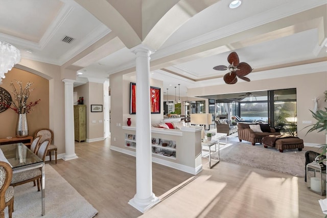 living room featuring ornamental molding, a ceiling fan, light wood finished floors, decorative columns, and a raised ceiling