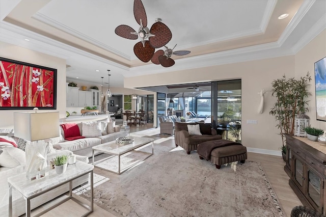 living area featuring baseboards, a tray ceiling, ornamental molding, ceiling fan, and light wood-type flooring