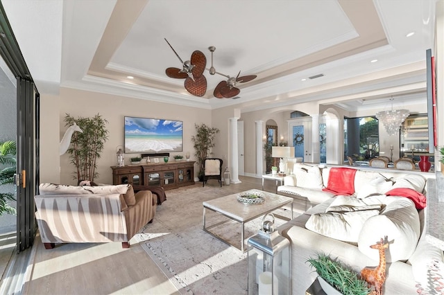 living room with ceiling fan, a tray ceiling, decorative columns, wood finished floors, and arched walkways