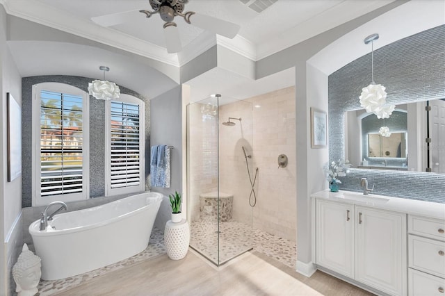 full bath with vanity, tiled shower, a soaking tub, ornamental molding, and ceiling fan with notable chandelier