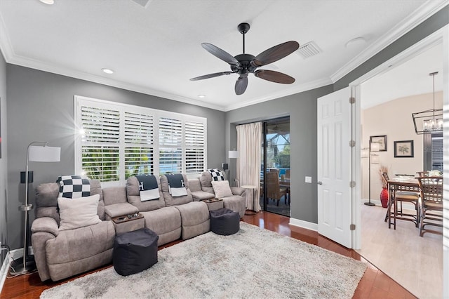 living area featuring visible vents, baseboards, ornamental molding, ceiling fan with notable chandelier, and wood finished floors