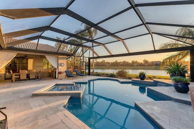 pool at dusk with a patio area, a pool with connected hot tub, a ceiling fan, and a water view