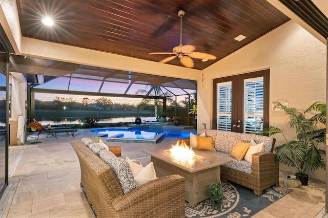 patio terrace at dusk featuring a water view, a ceiling fan, an outdoor living space with a fire pit, an outdoor pool, and a lanai