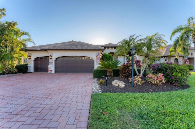 mediterranean / spanish home with a tiled roof, decorative driveway, an attached garage, and stucco siding