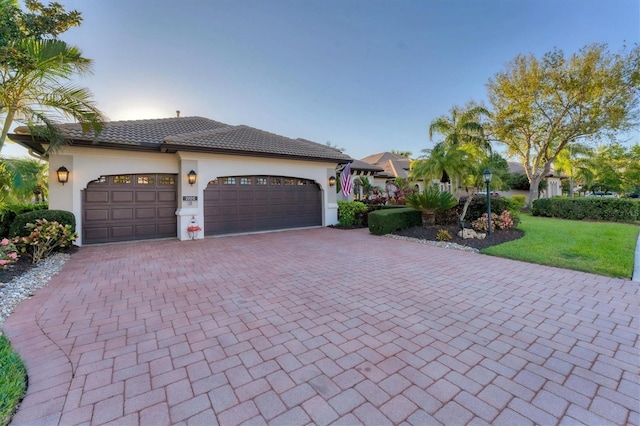 view of front of house with stucco siding, a front lawn, a tile roof, decorative driveway, and a garage