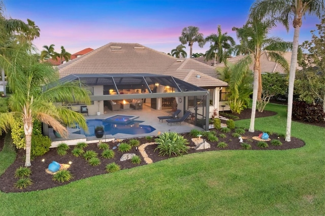 back of property at dusk featuring a lawn, a patio, glass enclosure, an in ground hot tub, and a tiled roof