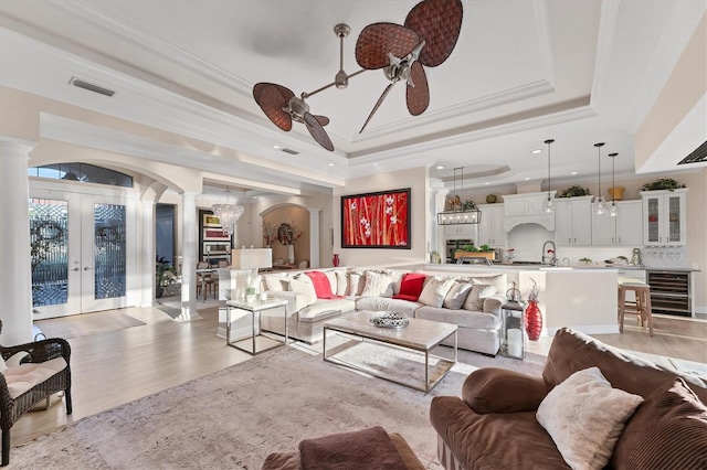 living area with a raised ceiling, wine cooler, arched walkways, and ornate columns