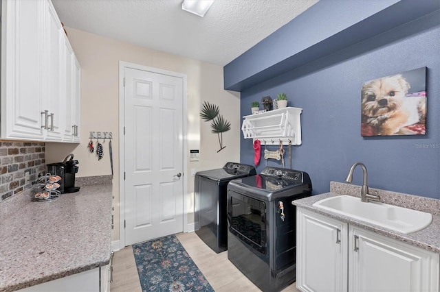 clothes washing area with washer and dryer, light wood-style floors, cabinet space, a textured ceiling, and a sink