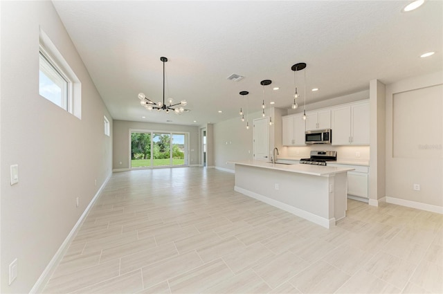 kitchen with a center island with sink, appliances with stainless steel finishes, open floor plan, light countertops, and white cabinetry