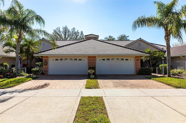 ranch-style home with a garage, decorative driveway, a tiled roof, and stucco siding