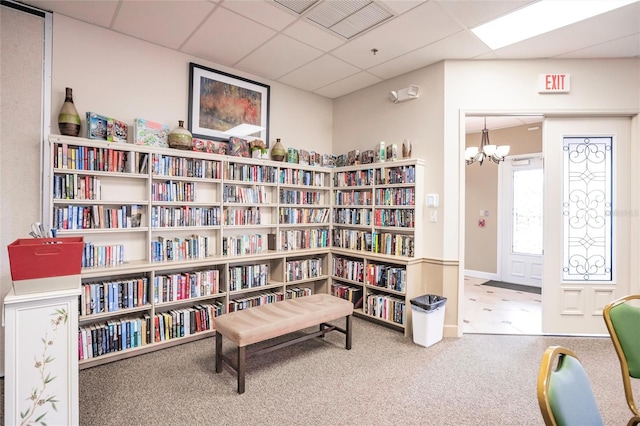 living area with carpet flooring, an inviting chandelier, wall of books, and a paneled ceiling