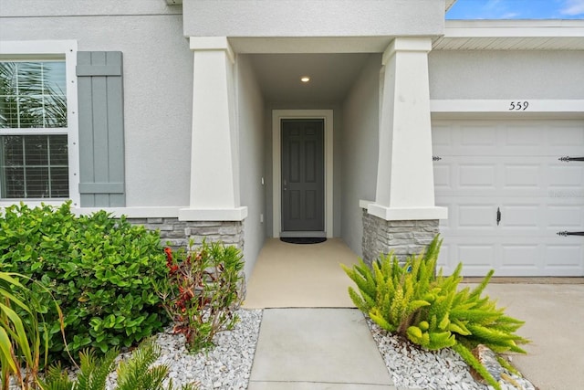 view of exterior entry with a garage, stone siding, and stucco siding