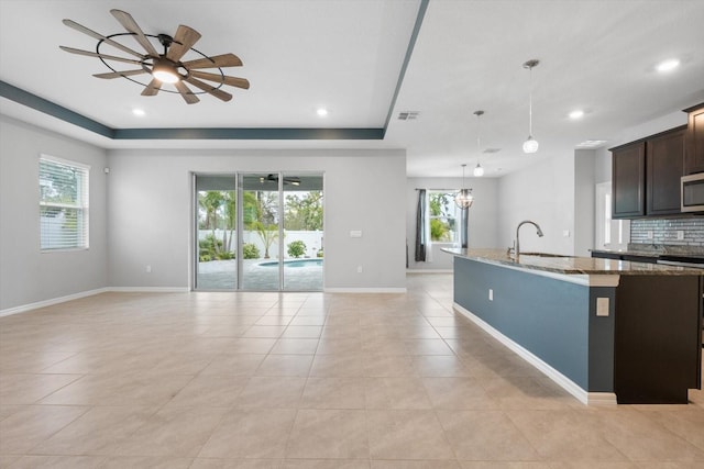 kitchen with decorative backsplash, an island with sink, stainless steel microwave, open floor plan, and a sink