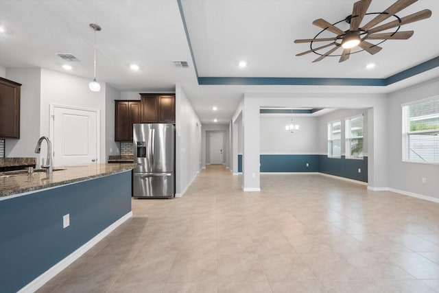 kitchen with dark brown cabinetry, stainless steel fridge, visible vents, dark stone counters, and a sink