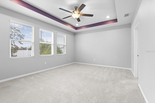 unfurnished room with a tray ceiling, visible vents, light carpet, ceiling fan, and baseboards