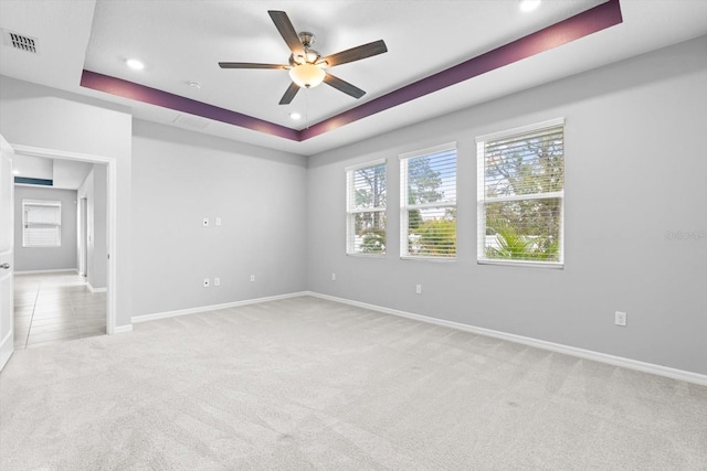 empty room featuring light carpet, a ceiling fan, visible vents, baseboards, and a tray ceiling