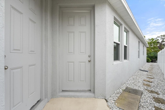 doorway to property featuring fence and stucco siding