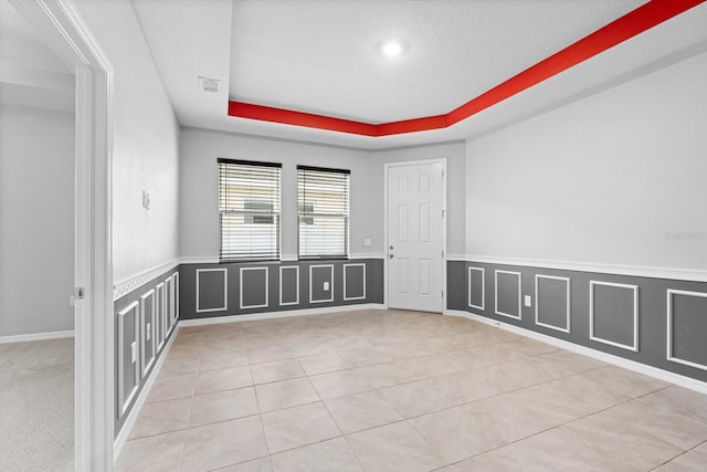 empty room featuring a raised ceiling, light tile patterned flooring, a decorative wall, and a wainscoted wall