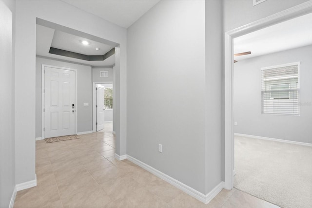 corridor with light carpet, plenty of natural light, a tray ceiling, and baseboards