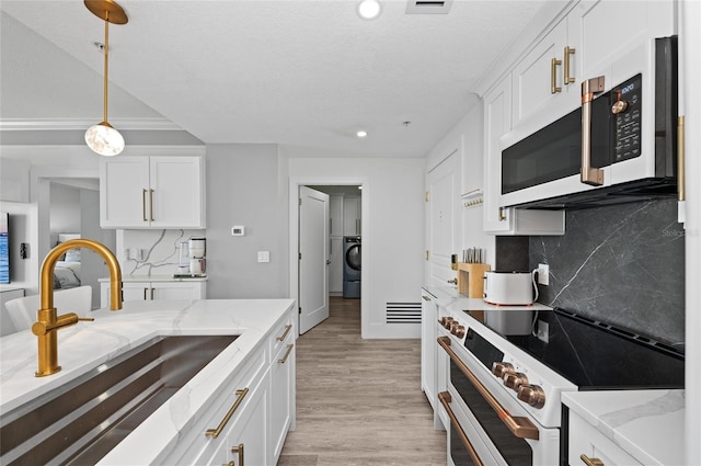 kitchen with white cabinetry, a sink, washer / dryer, light wood-type flooring, and white appliances