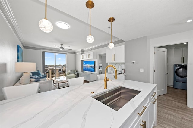 kitchen featuring a sink, white cabinets, open floor plan, washer / clothes dryer, and decorative light fixtures