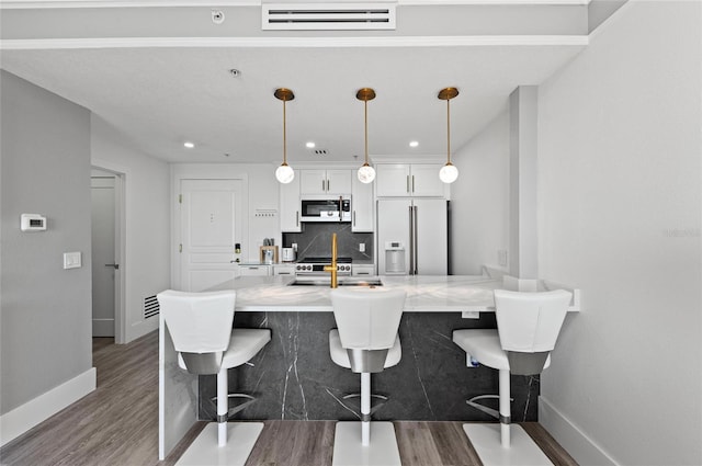 kitchen featuring high end fridge, tasteful backsplash, white cabinetry, and a kitchen breakfast bar