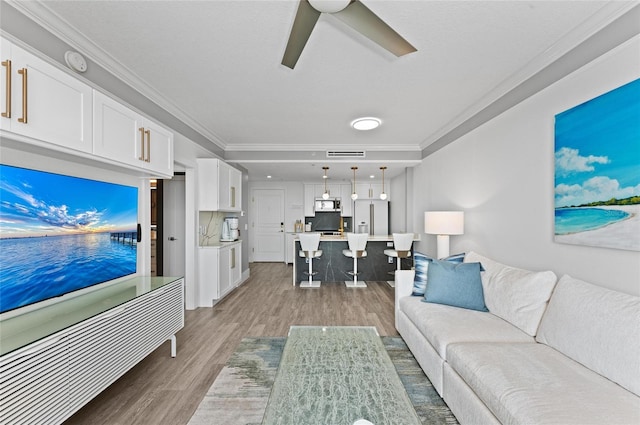 living room featuring light wood finished floors, visible vents, and crown molding