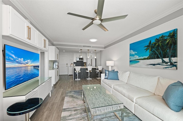 living area with ceiling fan, ornamental molding, wood finished floors, and visible vents