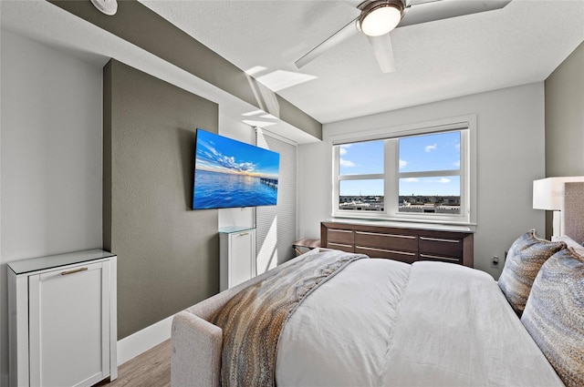 bedroom with a ceiling fan, a textured ceiling, baseboards, and wood finished floors