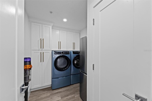 clothes washing area with wood finished floors, washing machine and dryer, cabinet space, and recessed lighting