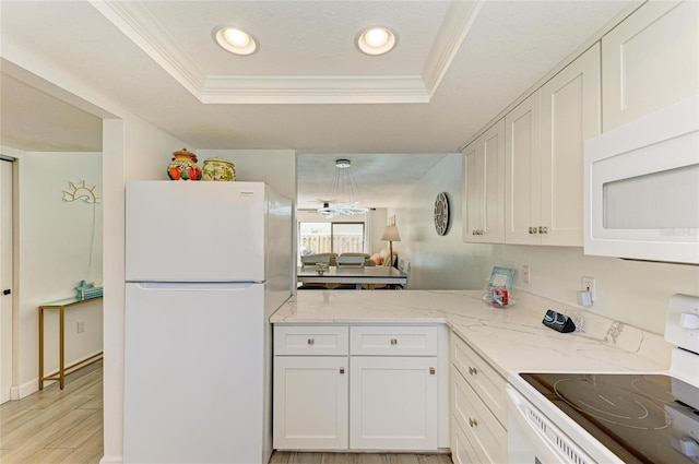 kitchen featuring white appliances, a raised ceiling, light wood-style flooring, light stone counters, and crown molding